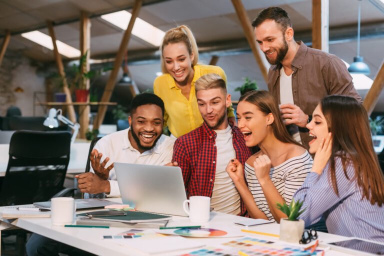 Team celebrating marketing results around a laptop in a modern office